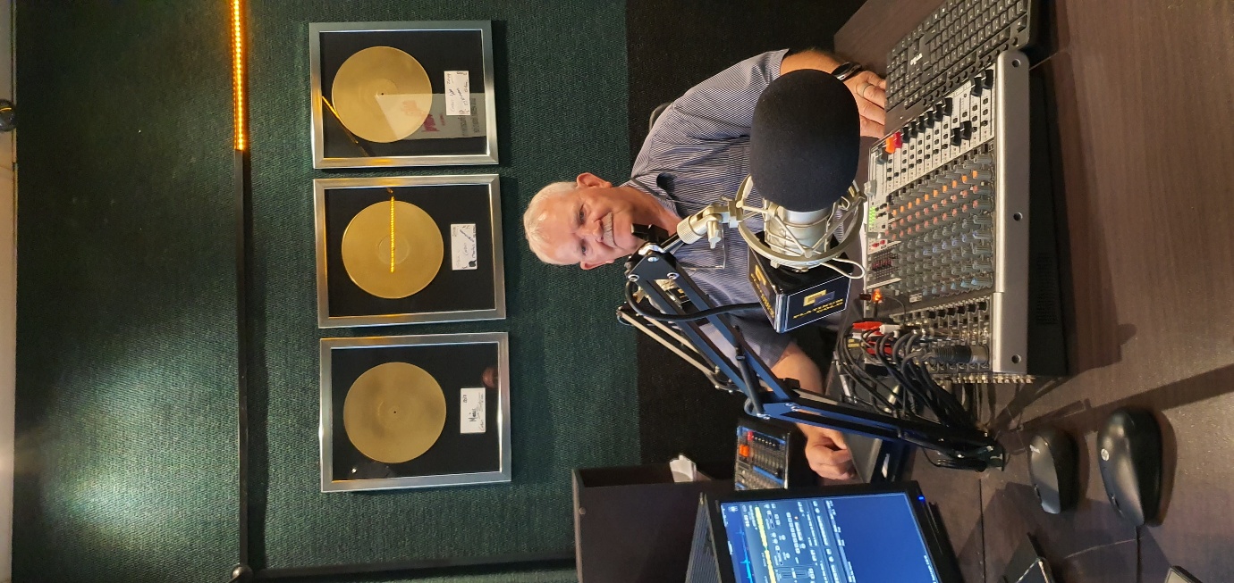 Bertie le Roux smiling behind the microphone and studio controls at Platinum Gold Radio